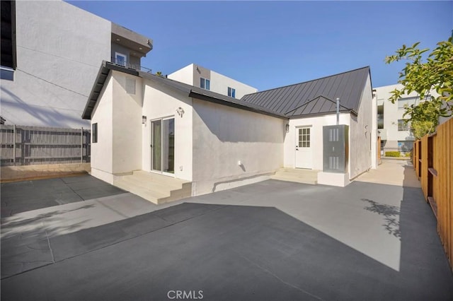 rear view of property with fence, stucco siding, a patio area, a standing seam roof, and metal roof