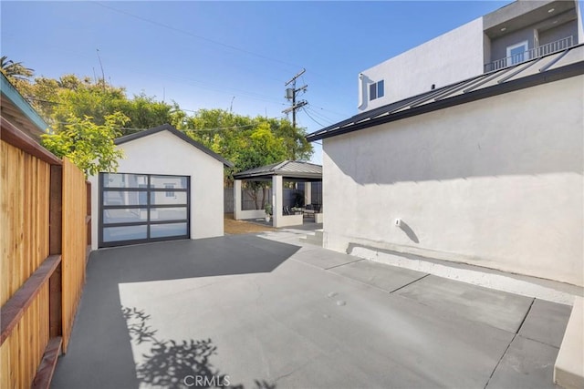 view of patio featuring driveway, an outbuilding, a garage, a gazebo, and fence
