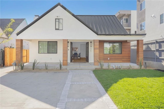 view of front of property with fence, a front yard, stucco siding, a standing seam roof, and metal roof