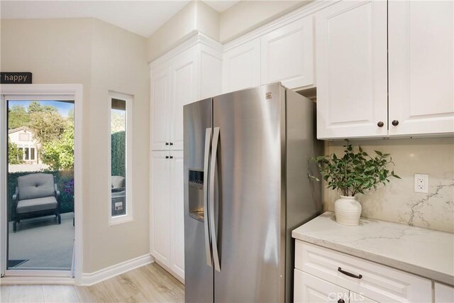kitchen with stainless steel fridge, light stone counters, baseboards, and white cabinetry
