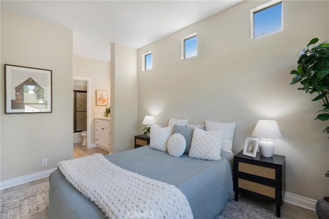 bedroom with ensuite bath, light wood finished floors, and baseboards