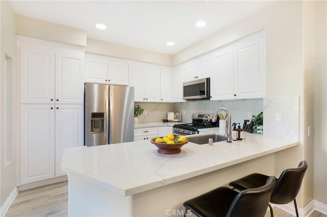 kitchen featuring light wood-type flooring, a peninsula, a breakfast bar, stainless steel appliances, and white cabinetry