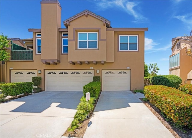 multi unit property with a garage, stucco siding, concrete driveway, and a chimney