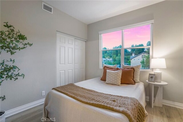bedroom featuring baseboards, visible vents, wood finished floors, and a closet