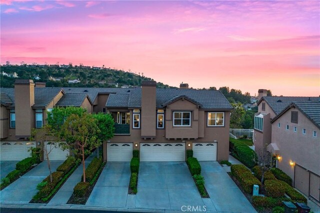 view of front of house with an attached garage, a tile roof, stucco siding, a chimney, and driveway