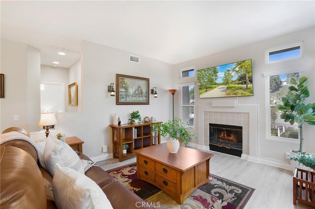 living room featuring light wood-style floors, visible vents, baseboards, and a tile fireplace