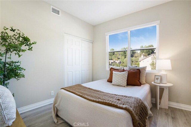 bedroom with visible vents, light wood-style flooring, baseboards, and a closet