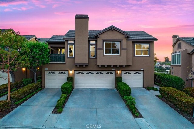 multi unit property with a tile roof, a garage, stucco siding, a chimney, and concrete driveway