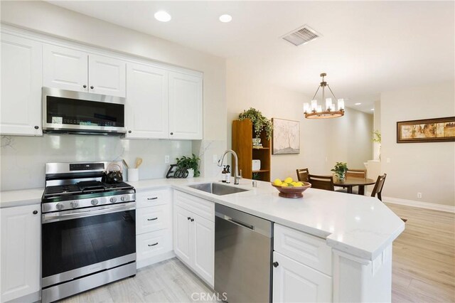 kitchen featuring visible vents, a sink, a peninsula, a chandelier, and stainless steel appliances