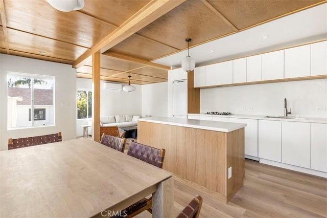 kitchen featuring a center island, black stovetop, wooden ceiling, a sink, and light wood-style flooring