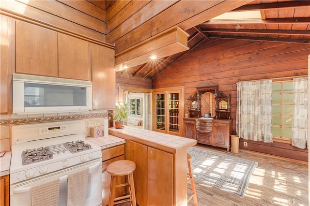 kitchen featuring lofted ceiling with beams, white appliances, tile counters, wood walls, and a peninsula