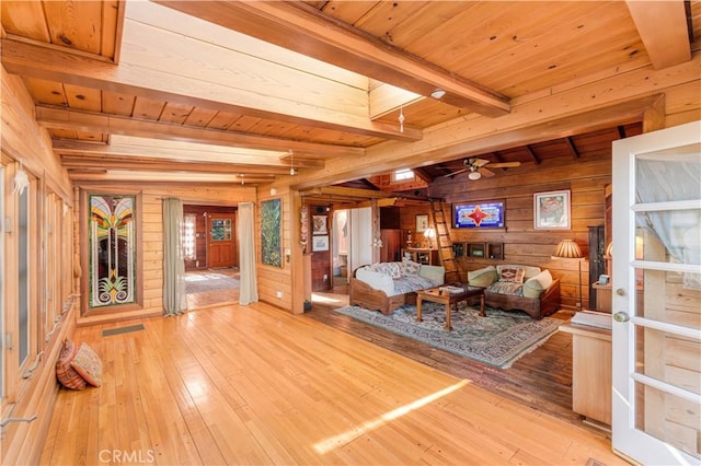 living room with wooden walls, ceiling fan, beam ceiling, and light wood-style flooring