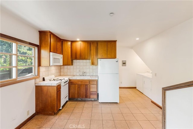 kitchen with brown cabinetry, tile countertops, tasteful backsplash, a sink, and white appliances