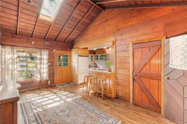 interior space featuring wood ceiling, lofted ceiling with beams, freestanding refrigerator, wooden walls, and light wood-style flooring