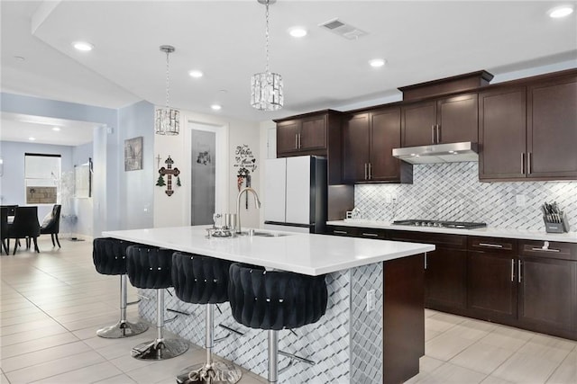 19183 Bension Dr, Saugus, CA 91350 - kitchen with freestanding refrigerator, under cabinet range hood, a breakfast bar area, light tile patterned floors, and backsplash