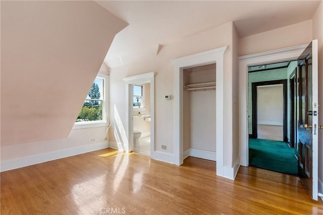 unfurnished bedroom with connected bathroom, baseboards, wood finished floors, and a closet