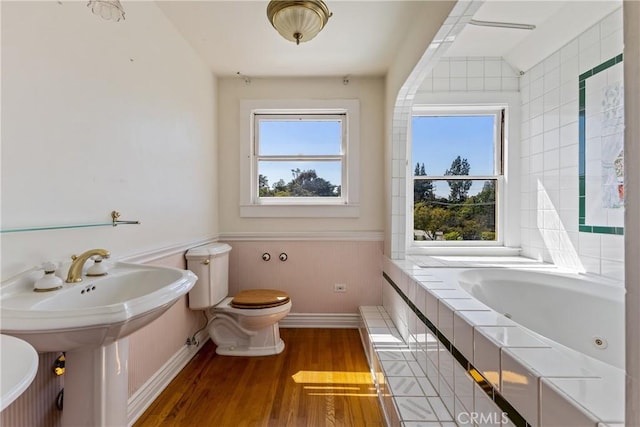 bathroom with a tub with jets, baseboards, wood finished floors, and toilet