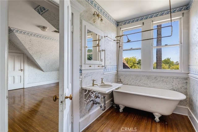 bathroom with a freestanding bath, baseboards, wallpapered walls, and wood finished floors