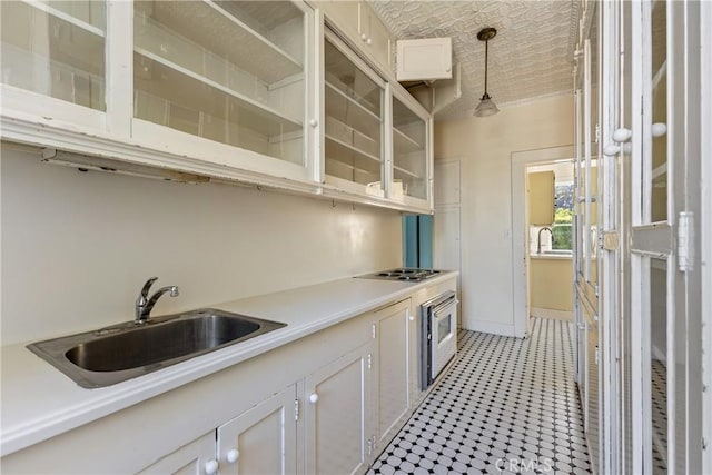 kitchen with stovetop, hanging light fixtures, a sink, light countertops, and baseboards