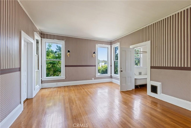 empty room featuring baseboards, wallpapered walls, wood finished floors, and visible vents