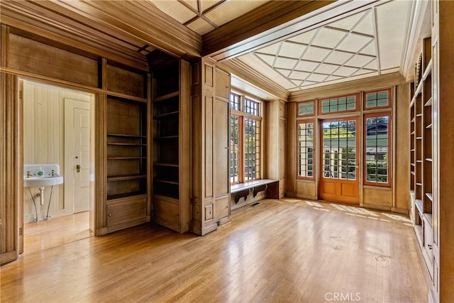 empty room featuring crown molding, wood walls, built in shelves, coffered ceiling, and light wood-style flooring