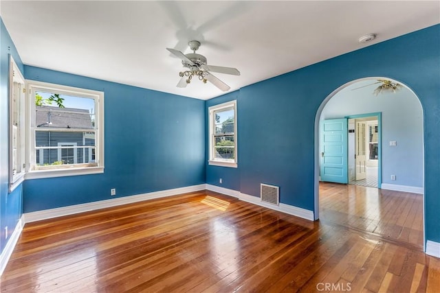 empty room with visible vents, arched walkways, baseboards, and hardwood / wood-style flooring