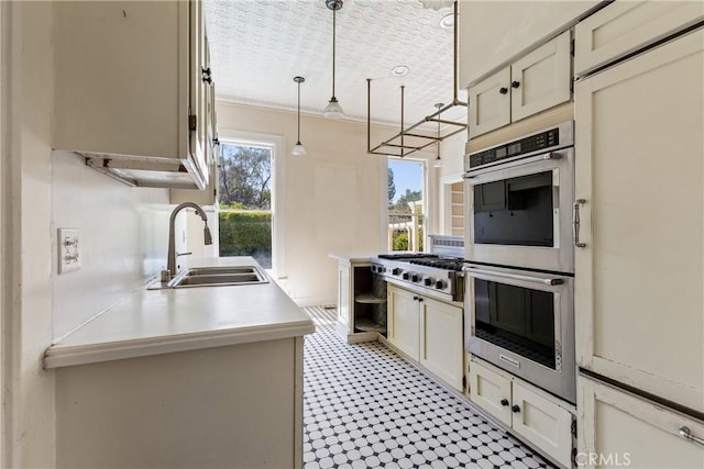 kitchen with appliances with stainless steel finishes, a sink, light countertops, decorative light fixtures, and light floors