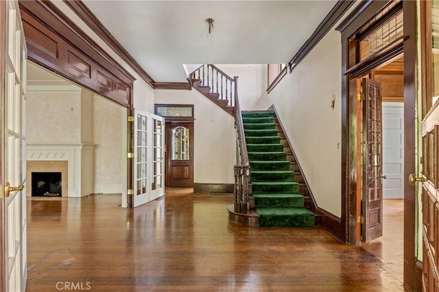 stairway featuring crown molding, a high ceiling, french doors, hardwood / wood-style floors, and a high end fireplace