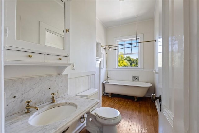 bathroom featuring crown molding, a freestanding tub, a sink, toilet, and hardwood / wood-style floors