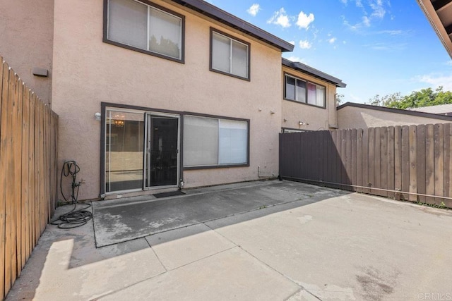 rear view of property featuring a patio, fence, and stucco siding