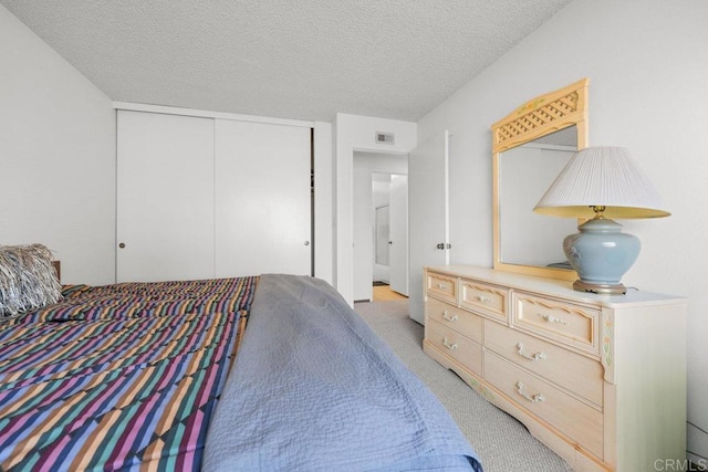 bedroom with a textured ceiling, light colored carpet, visible vents, and a closet