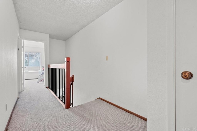 hall featuring carpet floors, a textured ceiling, and an upstairs landing