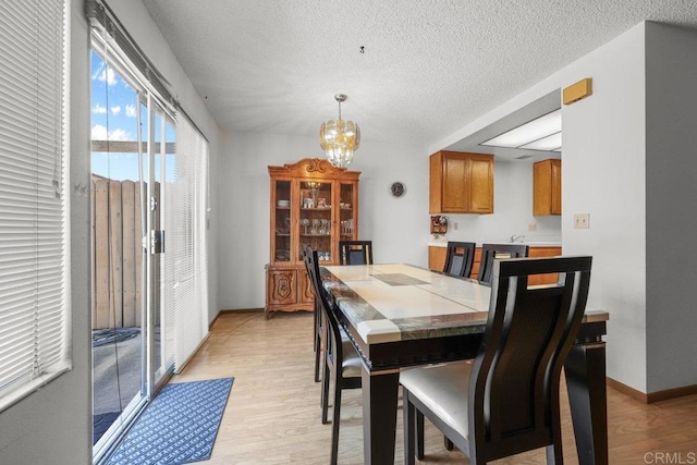 dining room featuring an inviting chandelier, a textured ceiling, baseboards, and light wood-type flooring