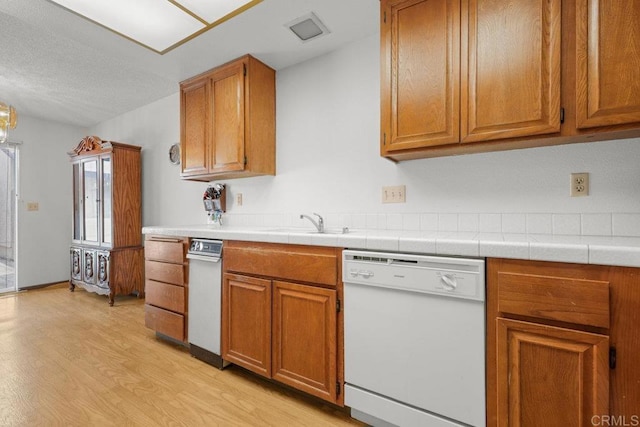 kitchen with brown cabinetry, light countertops, light wood finished floors, and dishwasher