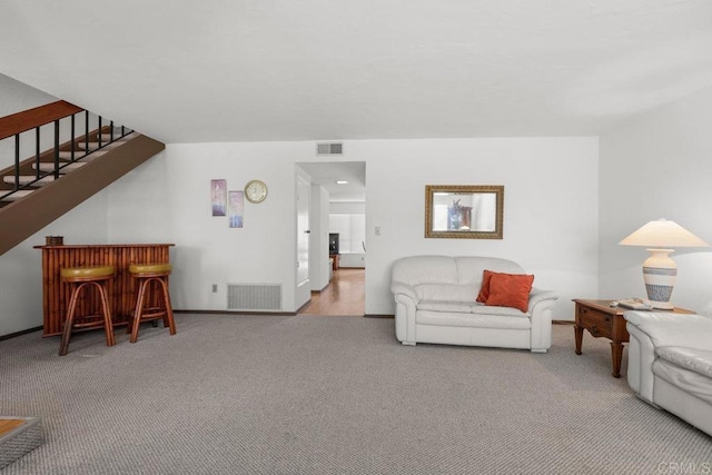 carpeted living area featuring visible vents, stairs, baseboards, and a bar