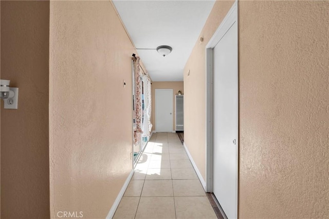 corridor featuring baseboards, a textured wall, and light tile patterned floors