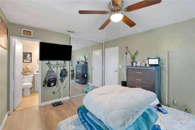 bedroom with ensuite bathroom, a ceiling fan, light wood finished floors, and visible vents
