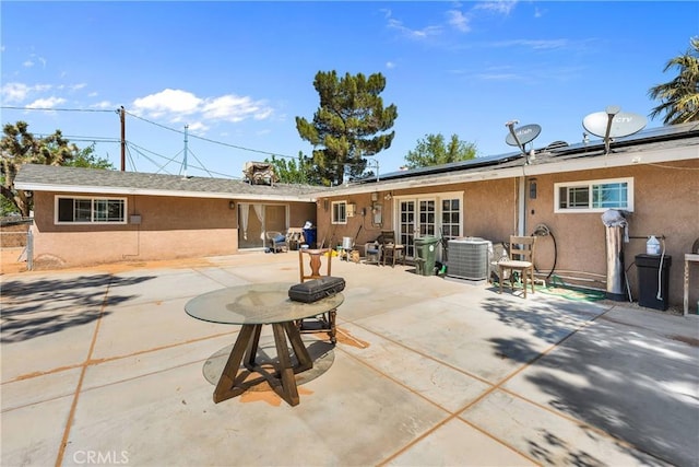 rear view of house featuring roof mounted solar panels, central air condition unit, stucco siding, and a patio area
