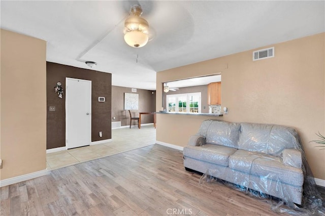 living room featuring baseboards, ceiling fan, visible vents, and light wood-style flooring