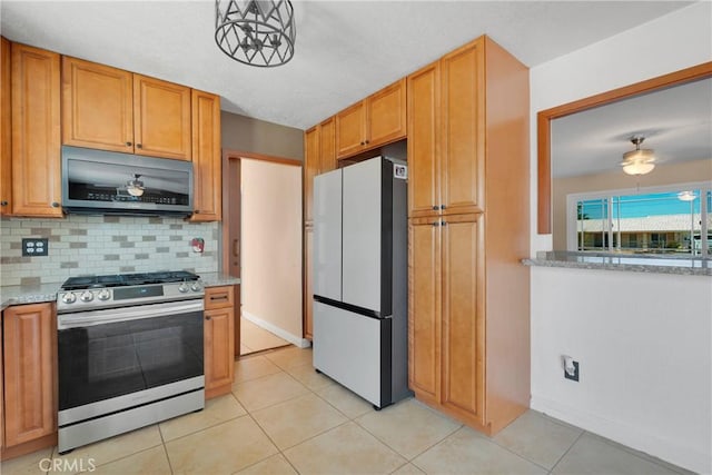 kitchen featuring tasteful backsplash, light tile patterned floors, baseboards, stainless steel gas range, and freestanding refrigerator