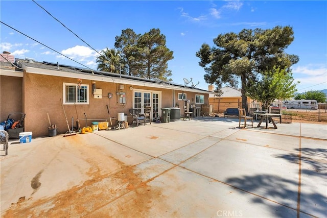 rear view of property with fence, french doors, solar panels, and stucco siding