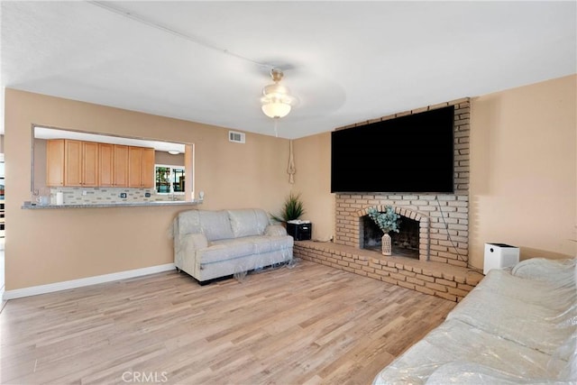 living area featuring a brick fireplace, visible vents, and wood finished floors