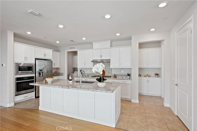 kitchen with a center island with sink, a sink, white cabinets, under cabinet range hood, and stainless steel appliances