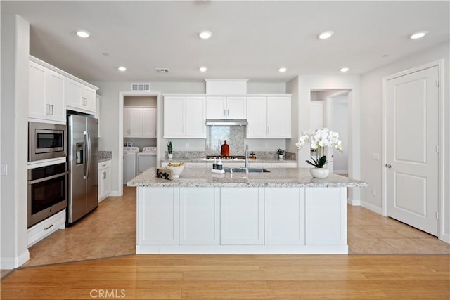 kitchen with washing machine and clothes dryer, light tile patterned flooring, appliances with stainless steel finishes, white cabinetry, and under cabinet range hood
