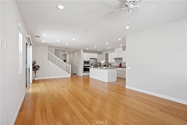 unfurnished living room with baseboards, light wood-style floors, ceiling fan, stairway, and recessed lighting