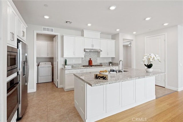 kitchen featuring visible vents, washer / clothes dryer, under cabinet range hood, a sink, and stainless steel appliances