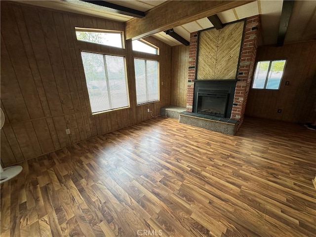 unfurnished living room featuring wooden walls, vaulted ceiling with beams, a fireplace, and wood finished floors