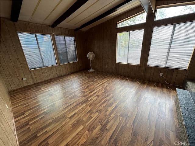 spare room with wood walls, vaulted ceiling with beams, and wood finished floors