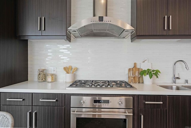 kitchen featuring dark brown cabinets, ventilation hood, a sink, backsplash, and stainless steel appliances