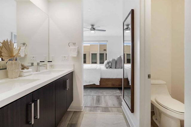 ensuite bathroom with a sink, ensuite bath, toilet, a ceiling fan, and wood finished floors
